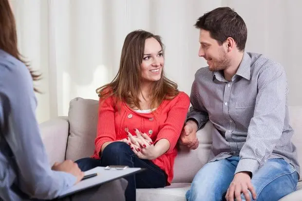 A man and woman sitting on the couch talking to another man.